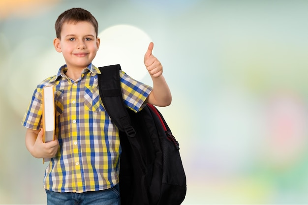 Niño de escuela con libro y mochila mostrando el pulgar hacia arriba