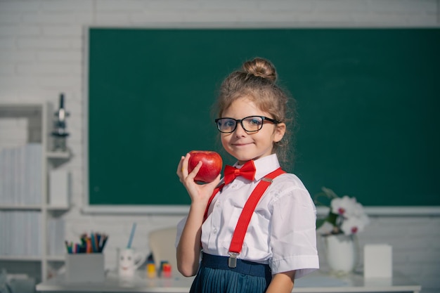 Niño de la escuela mantenga manzana con expresión divertida contra la pizarra Educación y conocimiento de los niños