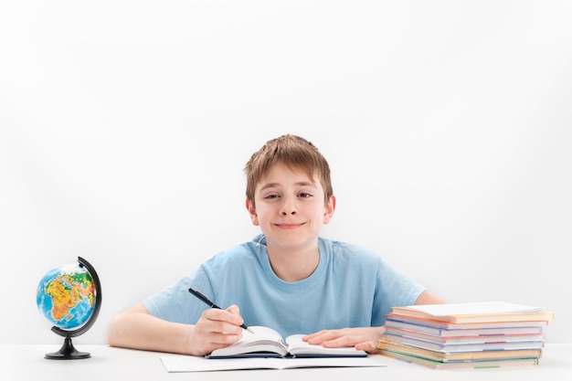 El niño de la escuela media hace la tarea El colegial se sienta a la mesa con el cuaderno y el globo aislado en el fondo blanco