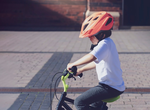 Niño de la escuela montando bicicleta en un casco, Niño de tiro corto aprende a andar en bicicleta en el parque, foto sincera Niño en casco montando en bicicleta en la carretera.