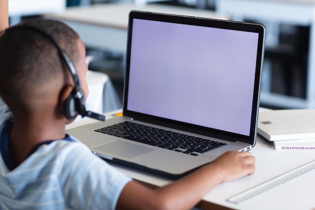 Niño de escuela primaria afroamericano con auriculares mientras usa una computadora portátil con espacio para copiar