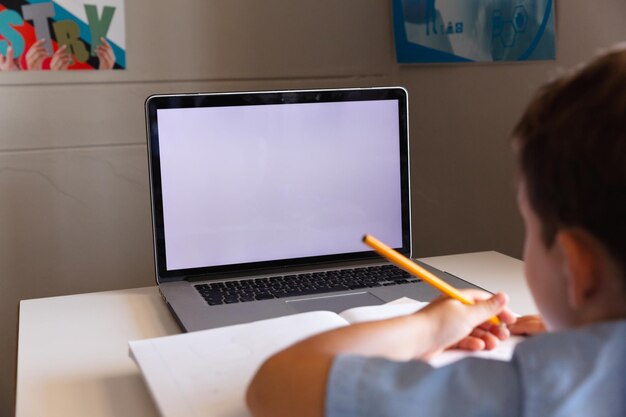 Niño de escuela primaria caucásico usando una computadora portátil mientras estudia en el escritorio de la escuela