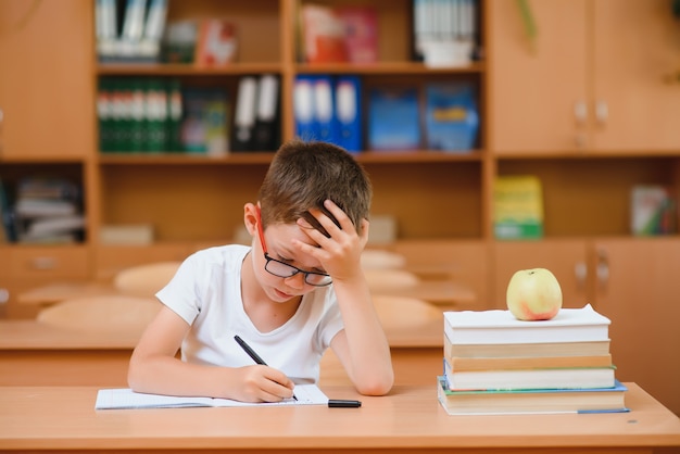 Niño de escuela primaria en el escritorio del aula tratando de encontrar nuevas ideas para el trabajo escolar.