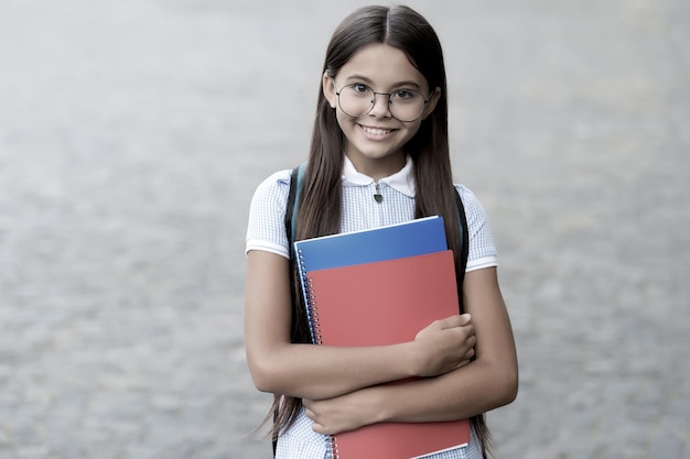 Niño de escuela primaria feliz sonrisa en anteojos sosteniendo libros al aire libre filtro vintage regreso a la escuela