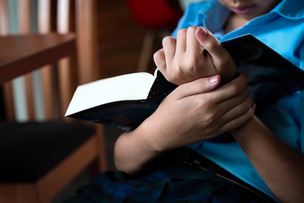 Niño de escuela primaria lee y sostiene el libro grande en su mano.