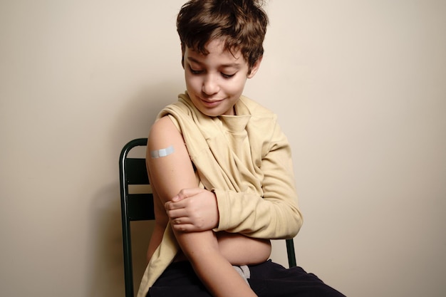 Niño de escuela primaria mostrando el brazo con una curita después de ser vacunado