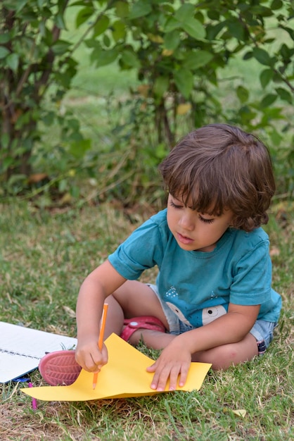 Niño de escuela primaria tirado en la hierba haciendo la tarea