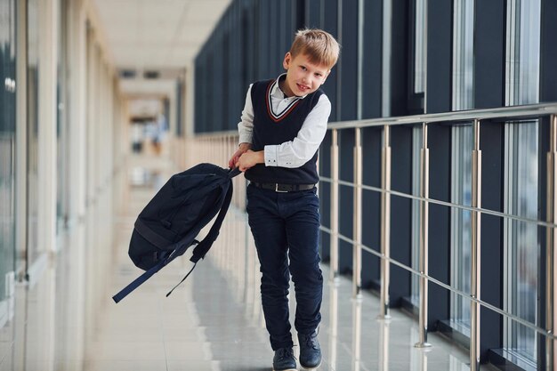 Niño de la escuela en uniforme caminando en el pasillo con mochila