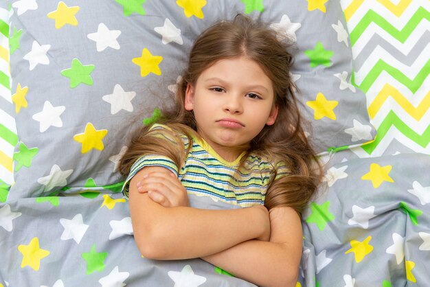 El niño está acostado en la cama y está indignado, no quiere levantarse para ir al colegio a estudiar.