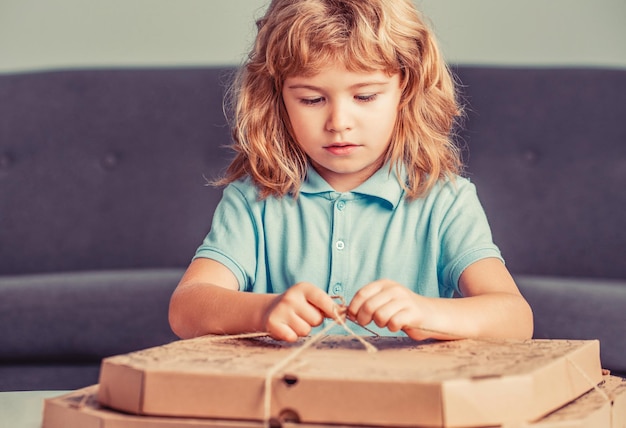 El niño está asombrado por una caja grande con enormes pizzas muy sorprendido y feliz Niño pequeño sosteniendo cajas de pizza Niño listo para comer una pizza Niño pequeño mirando una caja de pizzas