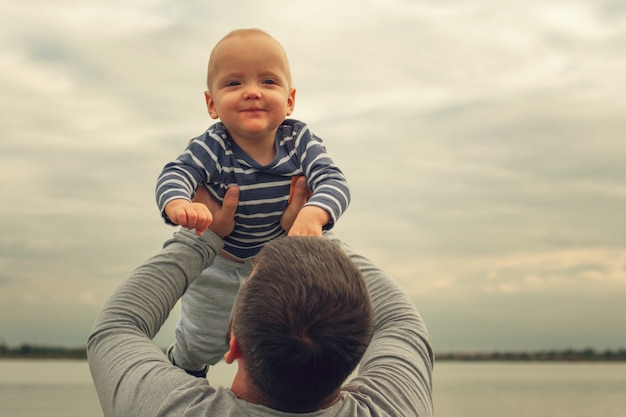 El niño está en brazos del padre. Niño contra el cielo de fondo en manos de papá.