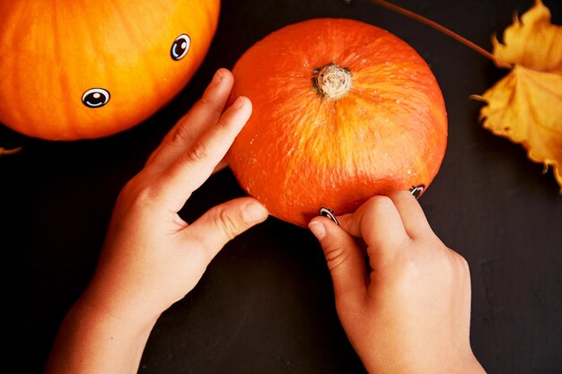 El niño está decorando una divertida calabaza con ojos para Halloween Decoraciones hechas a mano para las fiestas Creatividad infantil