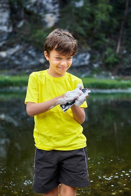 El niño está destruyendo el teléfono celular mientras lo lava en el río, está sonriendo.