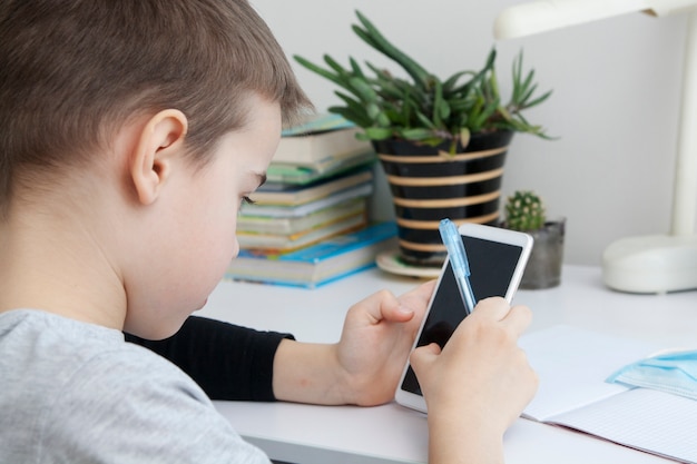 El niño está estudiando en casa en línea con un teléfono inteligente. Concepto de escolarización domiciliaria de cuarentena de coronavirus