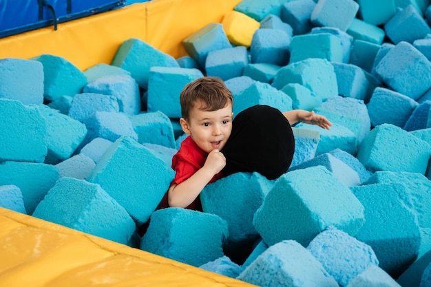 Un niño está jugando en una guardería de juegos. Juega con cubos grandes y suaves. Pasatiempo activo en el parque de diversiones Trampolines y una piscina seca.