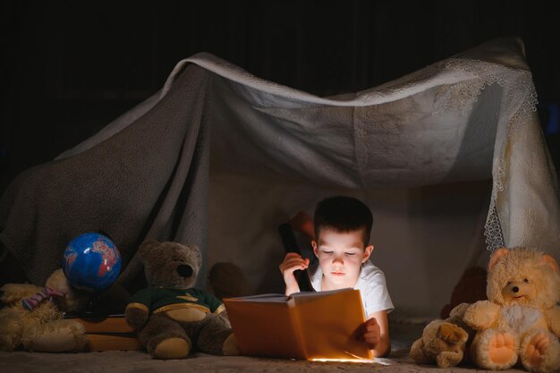 El niño está leyendo un libro con una linterna.