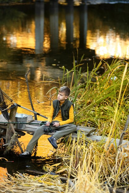 Niño está pescando al atardecer en el lago