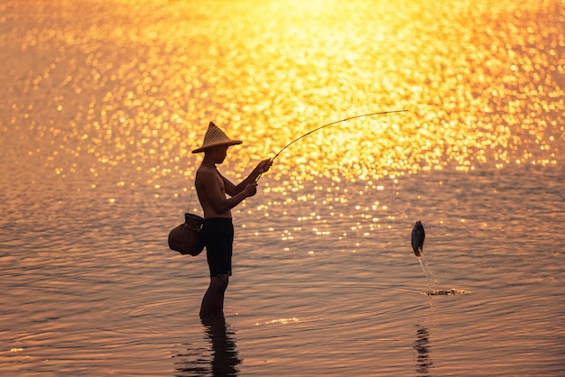 Niño está pescando al atardecer en el lago