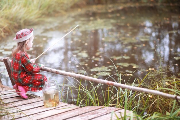 Un niño está pescando en la mañana de otoño. Atardecer de otoño en el estanque. Un pescador con una caña de pescar en la pasarela.