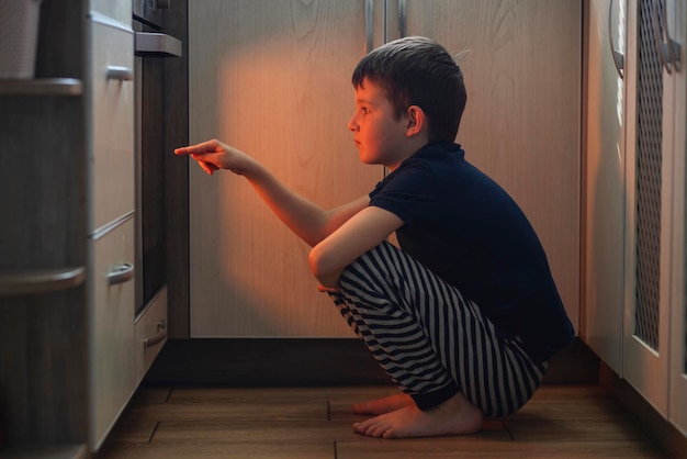 Un niño está sentado cerca del horno en la cocina y esperando
