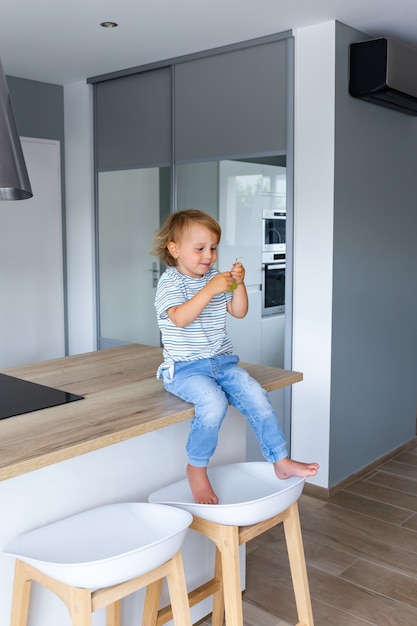 Niño está sentado en una mesa en la cocina y comiendo uvas. El niño está probando comida sana.