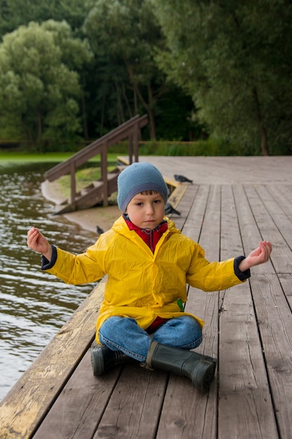 Un niño está sentado en un puente de madera con un impermeable amarillo. Un niño en un paseo