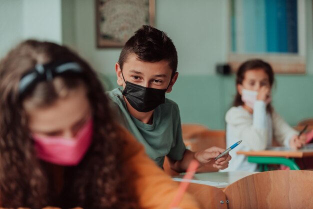 El niño está sentado en un pupitre escolar y lleva una máscara en la cara contra la protección contra el virus de la corona Nueva educación normal durante la pandemia de Covid19 Enfoque selectivo Foto de alta calidad