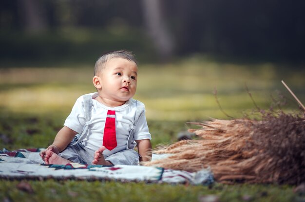 Un niño está sentado sobre un paño extendido sobre la hierba del parque. Niño de 6 meses.