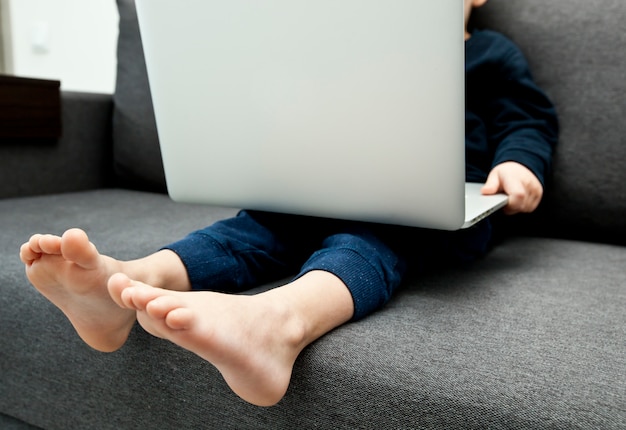 El niño está sentado en el sofá con laptop y mira dibujos animados