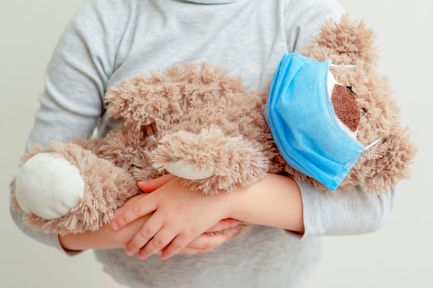 El niño está sosteniendo el oso del juguete en máscara médica.