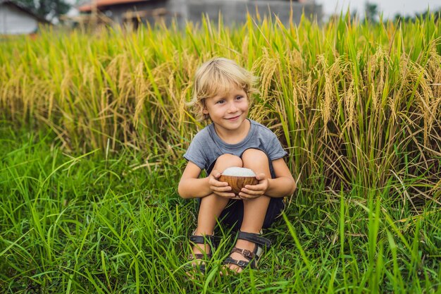 El niño está sosteniendo una taza de arroz hervido en una taza de madera en el fondo de un alimento de campo de arroz maduro para