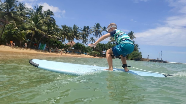 El niño está surfeando sobre las olas en el mar azul Playa de arena con hermosas palmerasxA