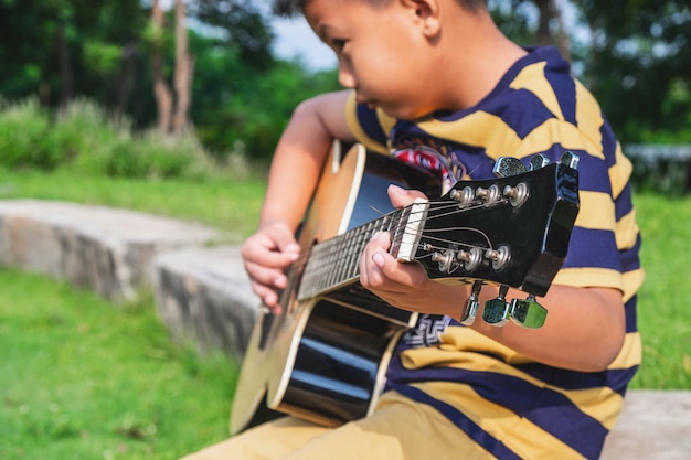 El niño está tocando la guitarra en el jardín.