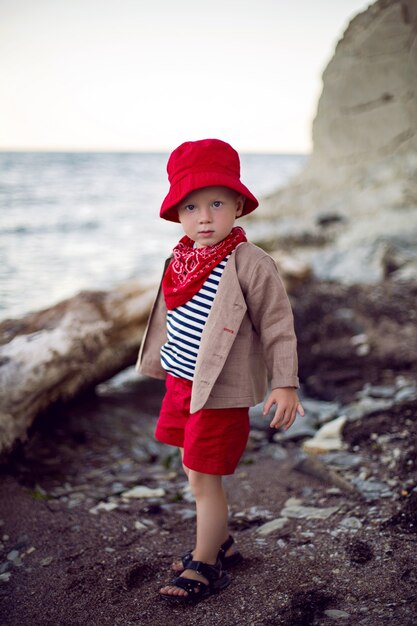 Niño con estilo en un chaleco se encuentra en una playa de guijarros junto al mar en verano