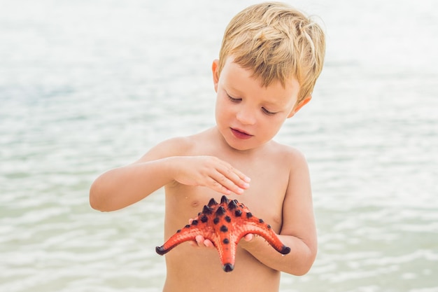 Un niño y una estrella de mar roja con el telón de fondo del mar.