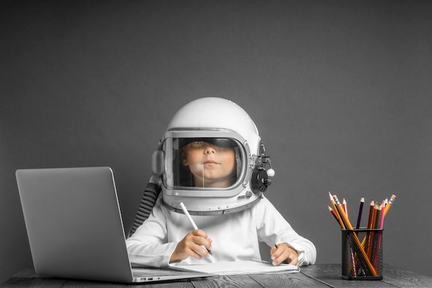 El niño estudia a distancia en la escuela, usando un casco de astronauta. De vuelta a la escuela