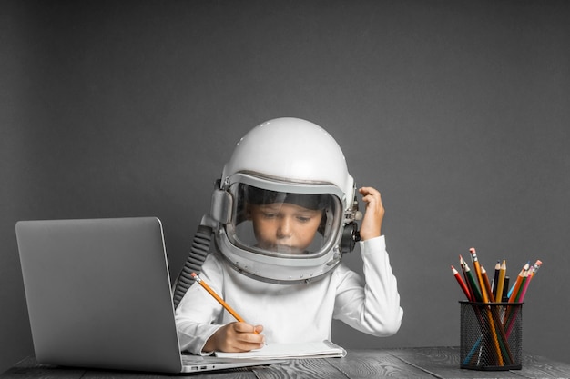 El niño estudia a distancia en la escuela usando un casco de astronauta