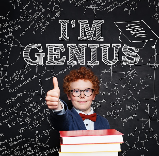 Foto niño estudiante con cabello rojo usando gafas en el aula contra la pizarra concepto de niño genio