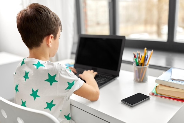 niño estudiante escribiendo en una computadora portátil en casa