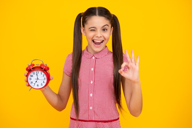 Foto niño estudiante niña con reloj aislado sobre fondo amarillo niño de regreso a la escuela concepto de educación y tiempo adolescente feliz emociones positivas y sonrientes de niña adolescente
