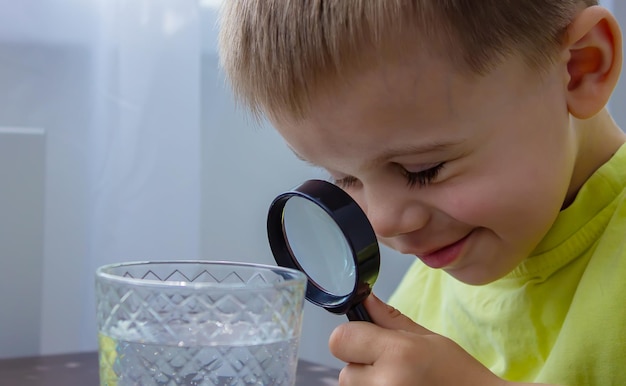 El niño examina el agua con una lupa en un vaso Enfoque selectivo