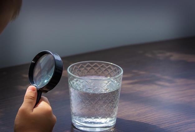 El niño examina el agua con una lupa en un vaso Enfoque selectivo