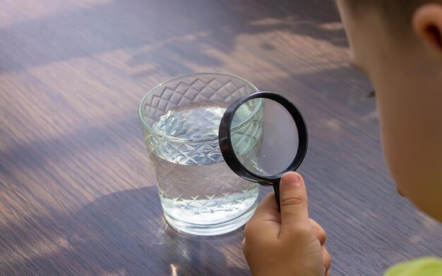 El niño examina el agua con una lupa en un vaso Enfoque selectivo