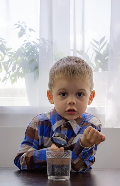 Foto el niño examina el agua con una lupa en un vaso enfoque selectivo