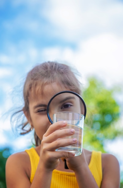 El niño examina un vaso de agua con una lupa. Enfoque selectivo.