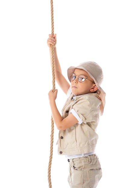 Niño explorador enfocado con sombrero y gafas sosteniendo una cuerda aislada en blanco