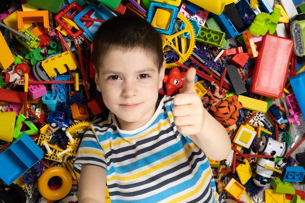 Niño feliz de 5 años mostrando los pulgares hacia arriba acostado entre los juguetes vista superior