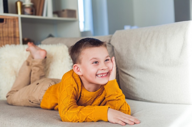 Niño feliz de 6 años está descansando en el sofá.