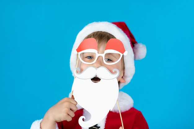 Niño feliz con accesorios de papel de Navidad contra la pared azul