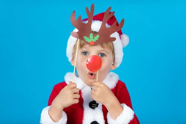 Niño feliz con accesorios de papel de Navidad contra la pared azul